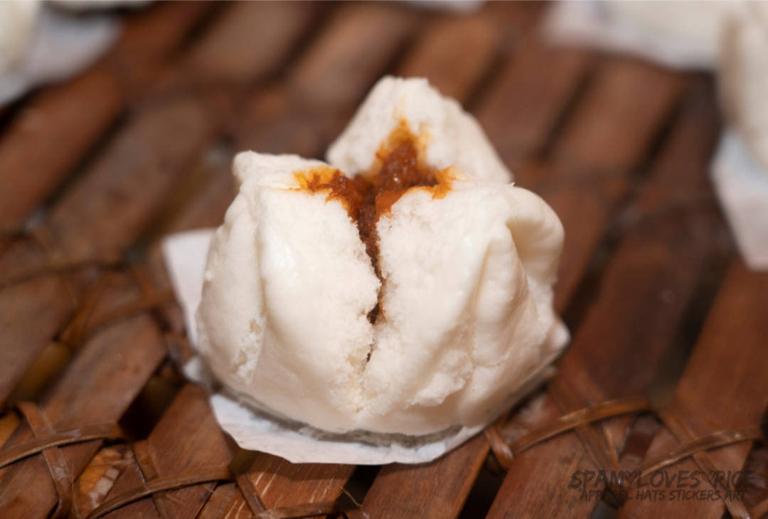 Freshly steamed Filipino siopao asado resting on a bamboo steamer, split open to reveal sweet braised pork filling